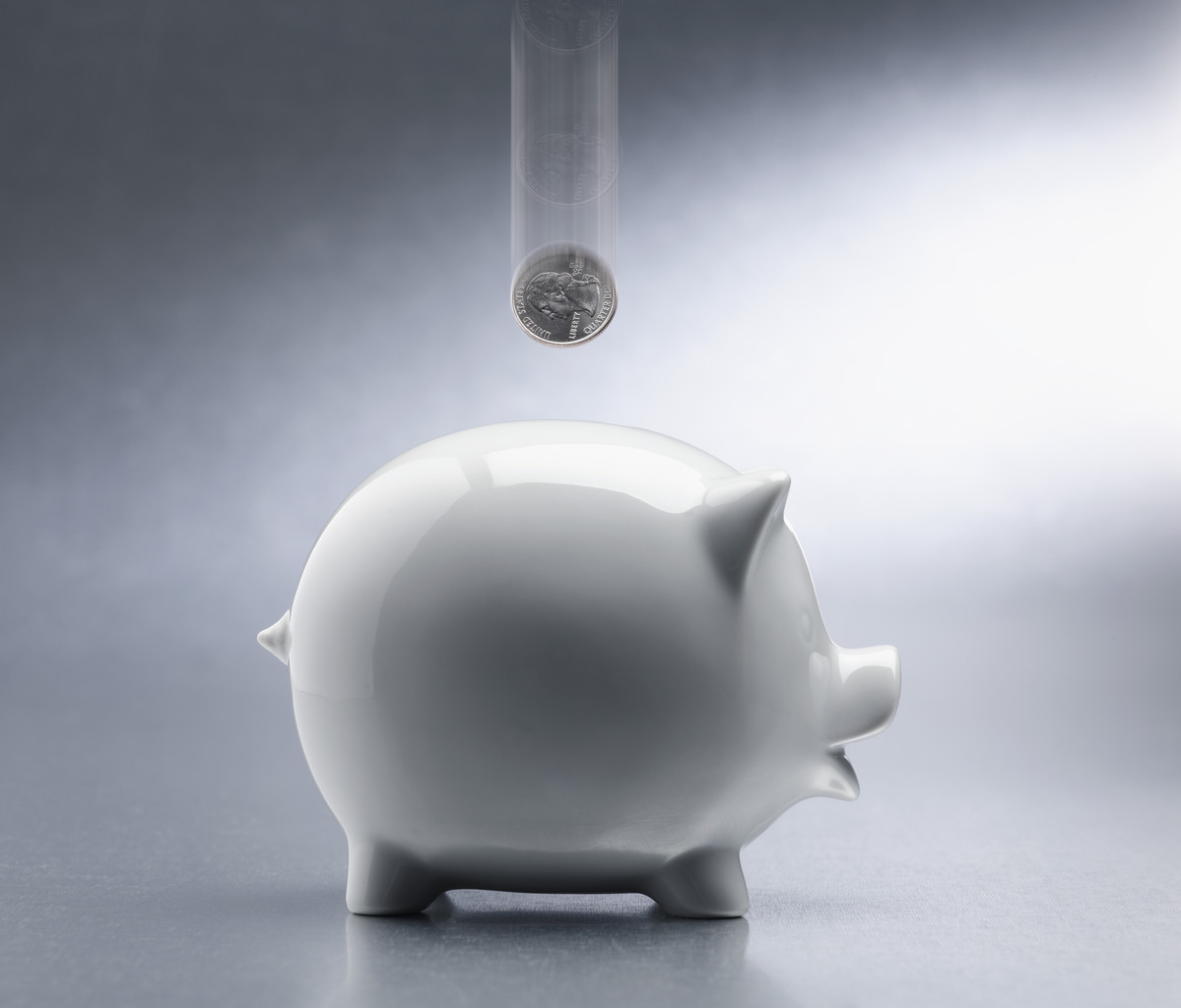 Quarter dropping into a piggy bank.